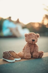brown bear plush toy beside pair of toddler s brown and white shoes on ground in selective focus photography