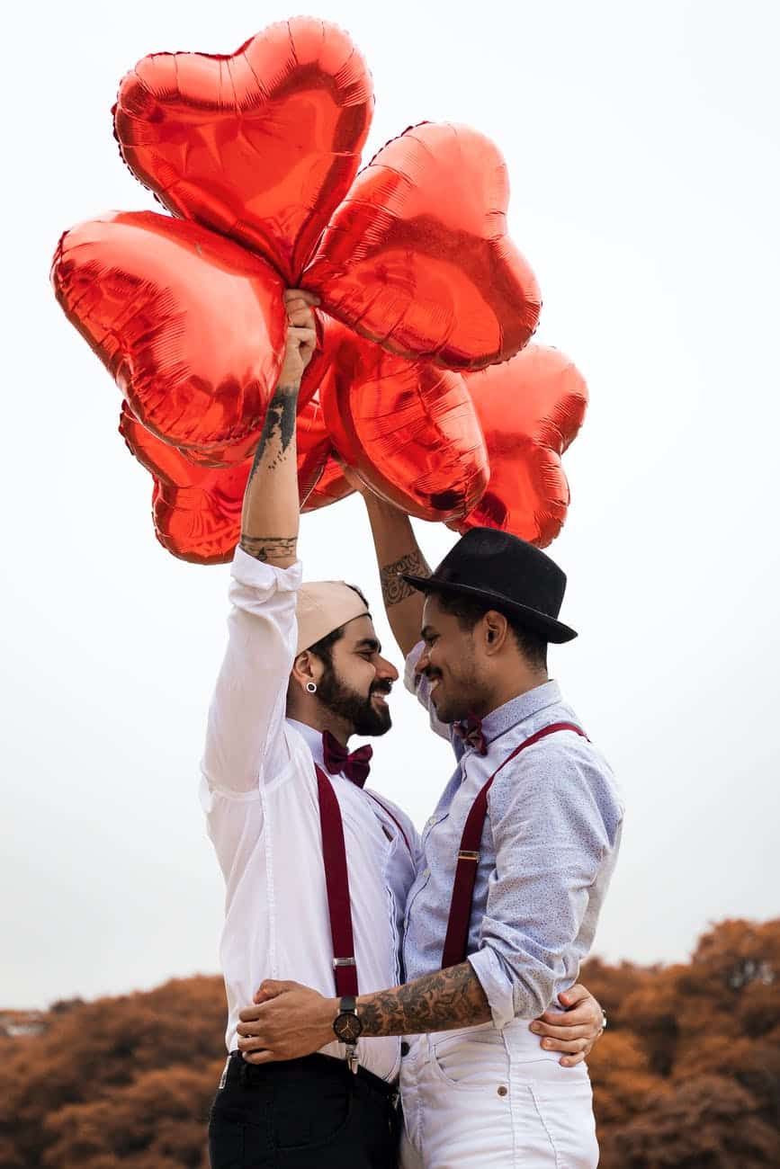 two men embracing while holding heart balloons