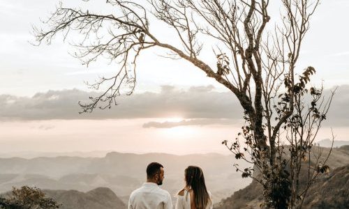 a couple in white dress standing in view of the mountain