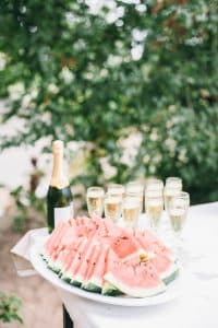 selective focus photo of bunch of sliced watermelons in white bowl near champagne bottle