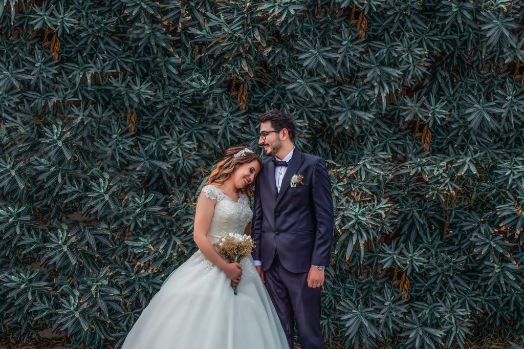 woman in white wedding dress holding bouquet of flowers leaning on man in black suit