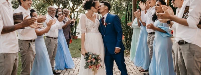 multiethnic couple kissing between smiling guests on wedding day