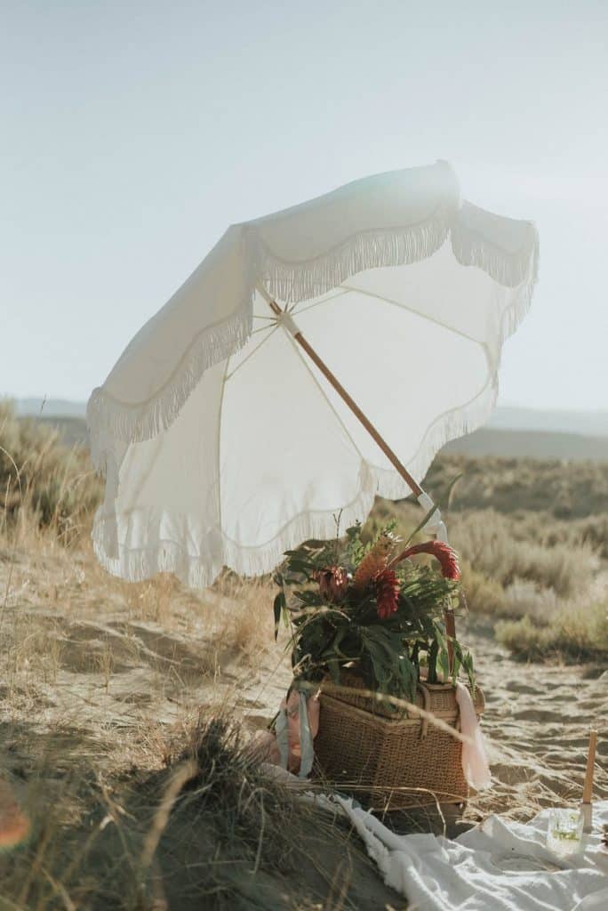 white umbrella and basket with flowers on sandy coast