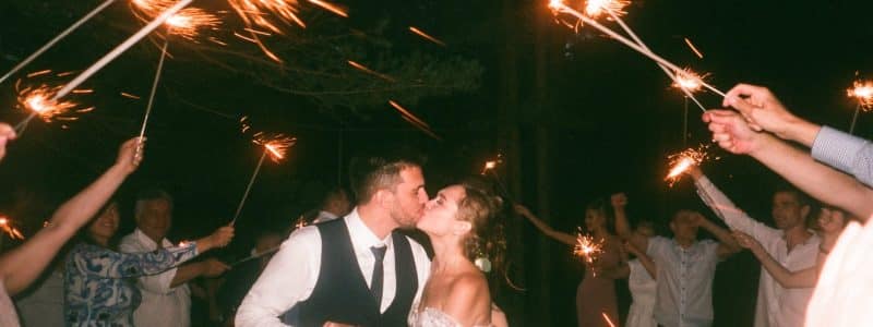 people raising lit sparklers while encircling bride and groom kissing