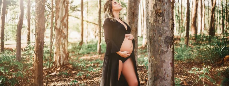 pregnant woman standing and touching her belly near trees