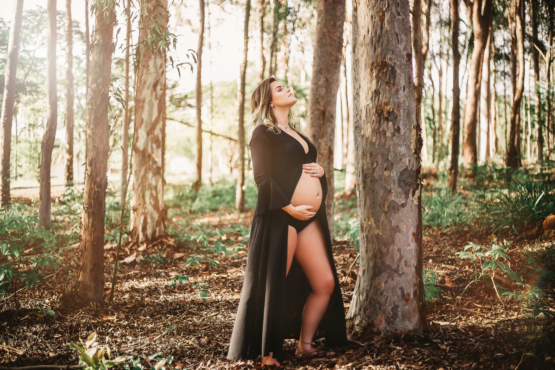pregnant woman standing and touching her belly near trees