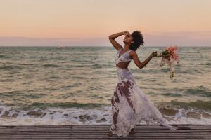 happy african american bride with flower bouquet near wavy ocean
