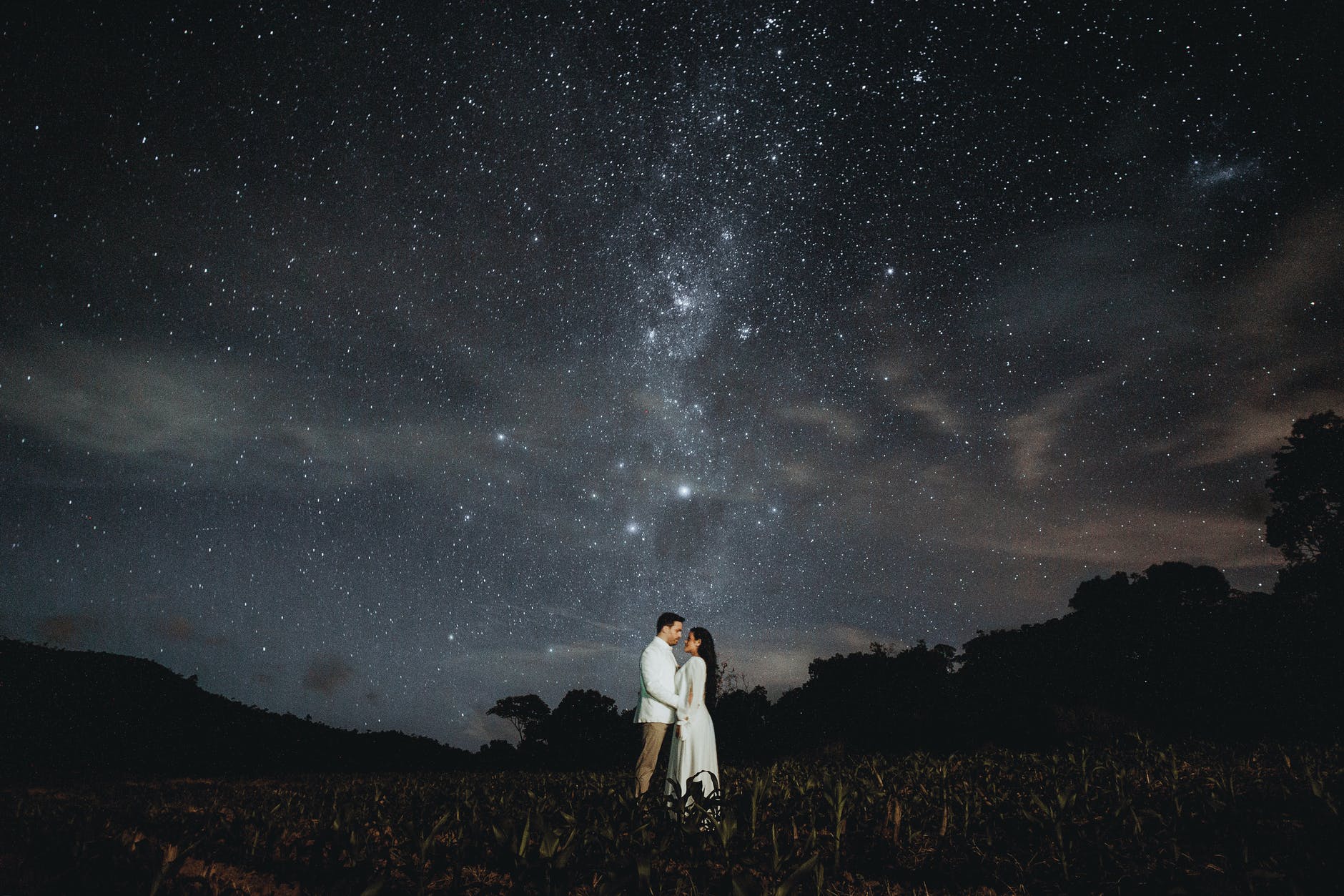 ethnic newlywed couple under starry sky in countryside