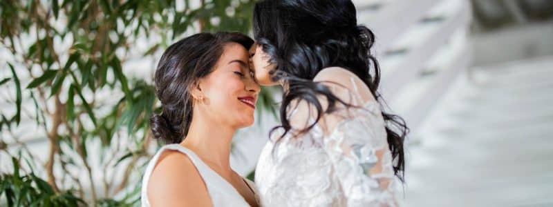 woman in white floral dress kissing woman in white dress