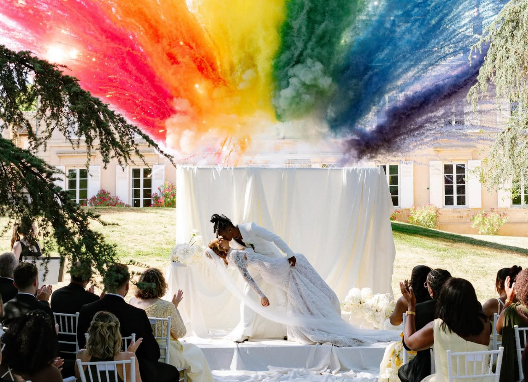photo de la fin de la cérémonie du mariage de Melvine Malard avec Justine où les mariées s'embrassent avec en fond un feu de jour coloré