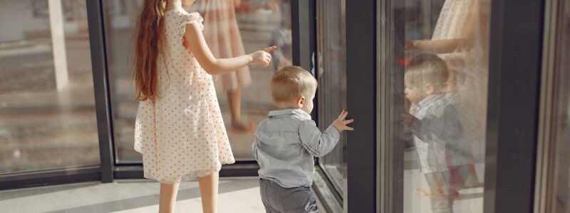 Un bébé avec sa grande soeur qui regardent à travers la fenêtre