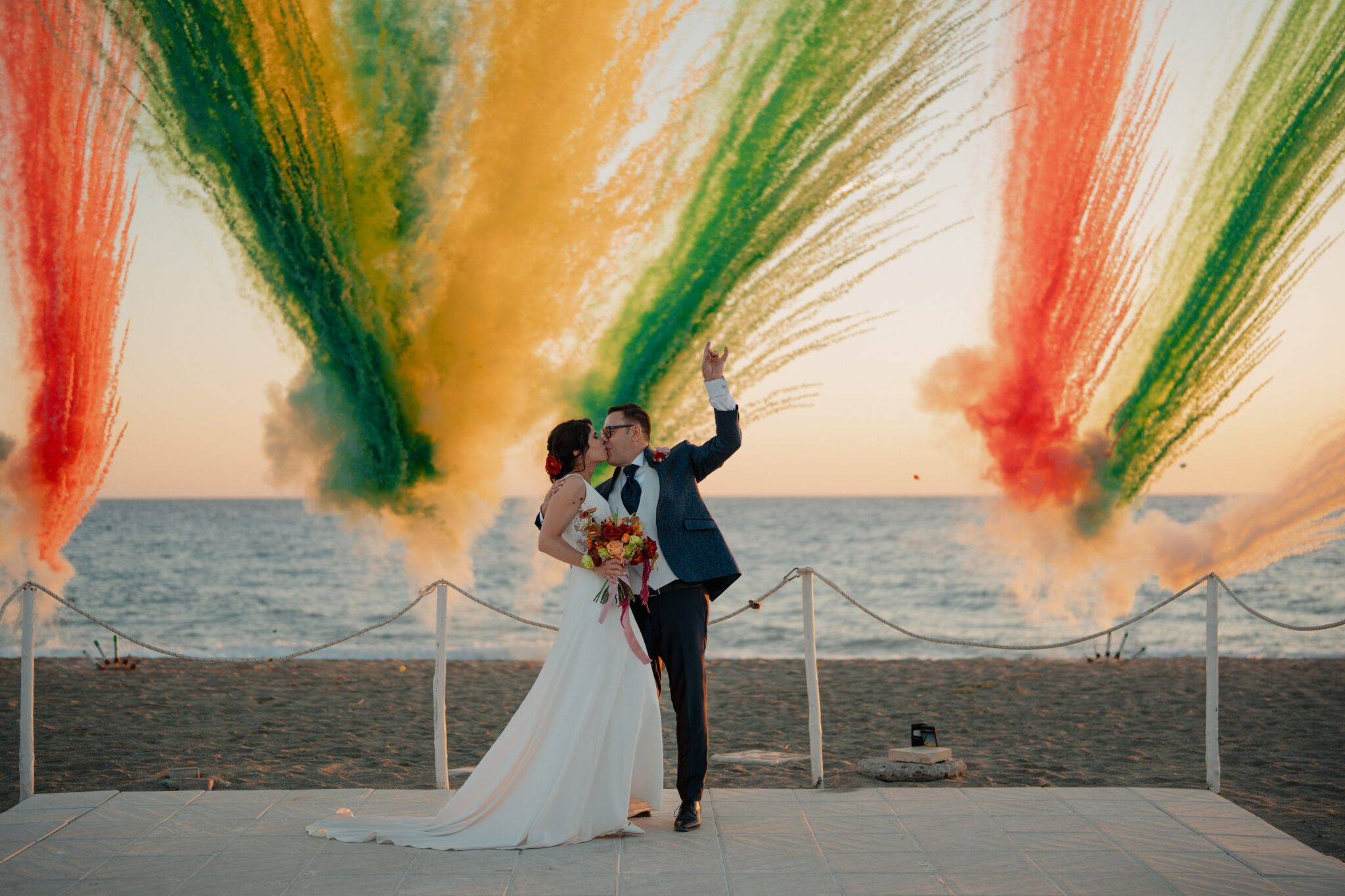 photo de mariés qui s'embrassent avec en fond un feu de jour coloré qui est une tendance actuelle dans les mariages