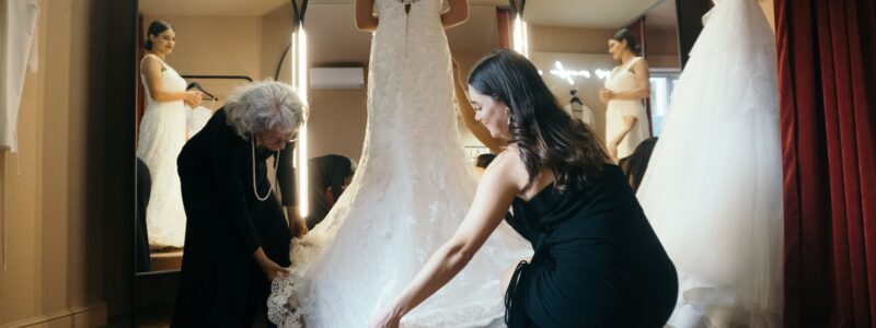Essayage de robe de mariée dans une boutique avec les vendeuses qui ajustent la robe et la traine pour que la mariée puisse se découvrir