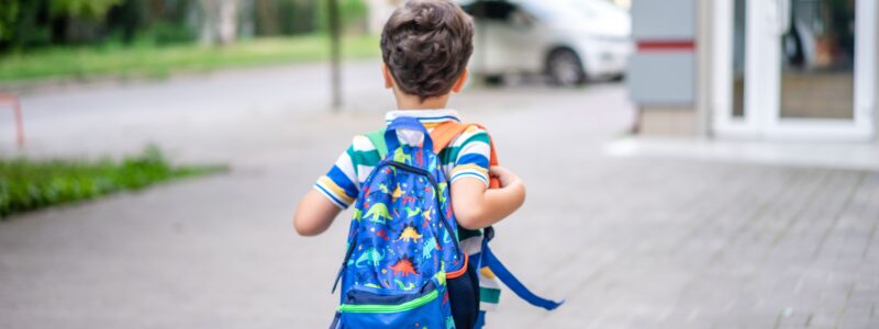 enfant qui va faire sa première rentrée en maternelle avec son sac à dos sur le dos et qui se dirige vers sa nouvelle école