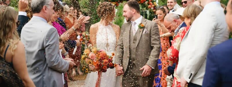 photo d'un couple qui sort de sa cérémonie laïque sous une pluie de pétales et entourés de leurs invités